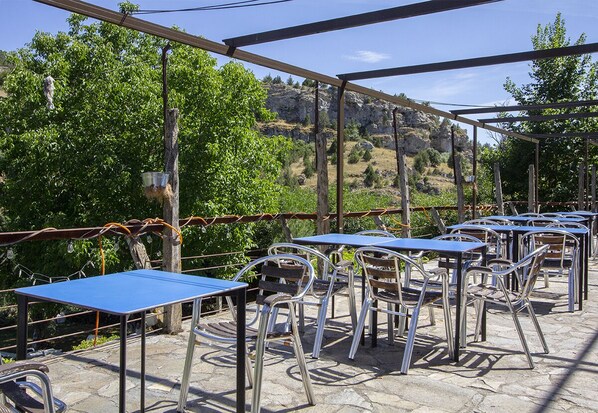 An outdoor patio with tables and chairs, a pergola structure, and a mountainous backdrop.