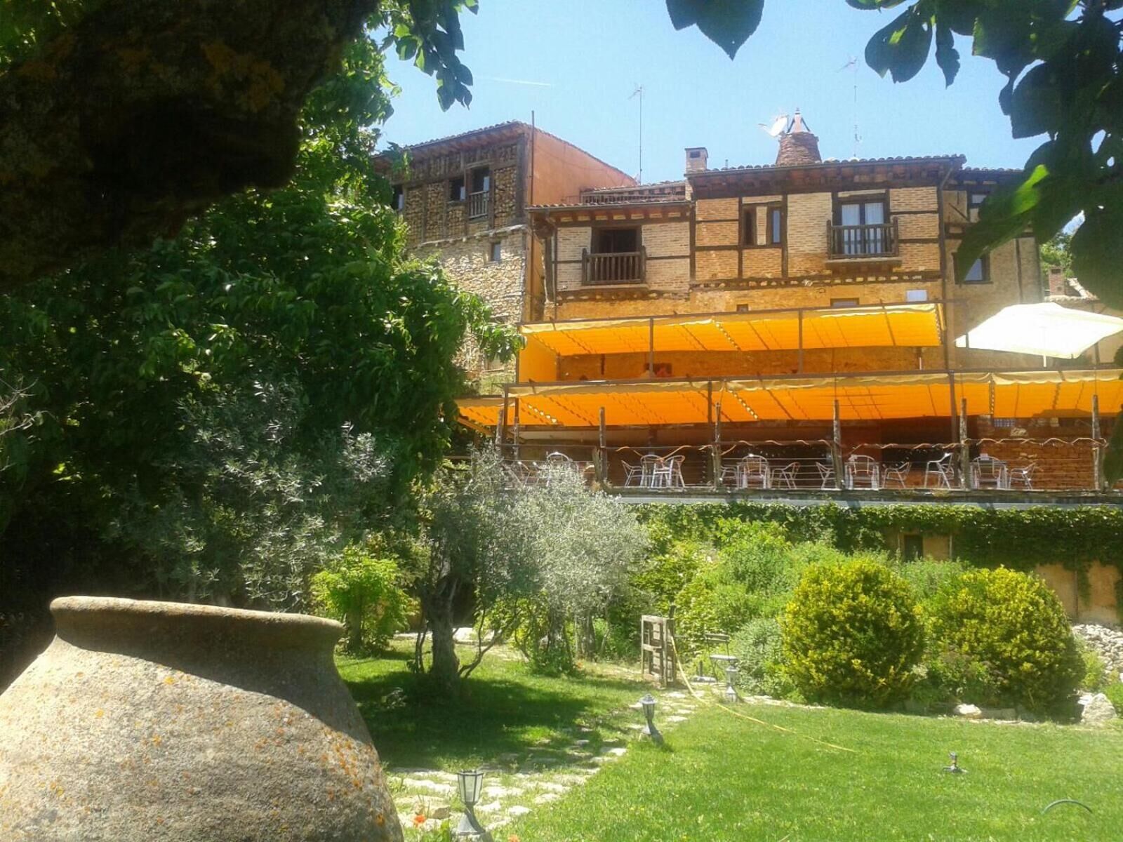 Un pati amb una gerra de pedra, un jardí petit i un edifici amb tenda groga i seients a l'aire lliure.