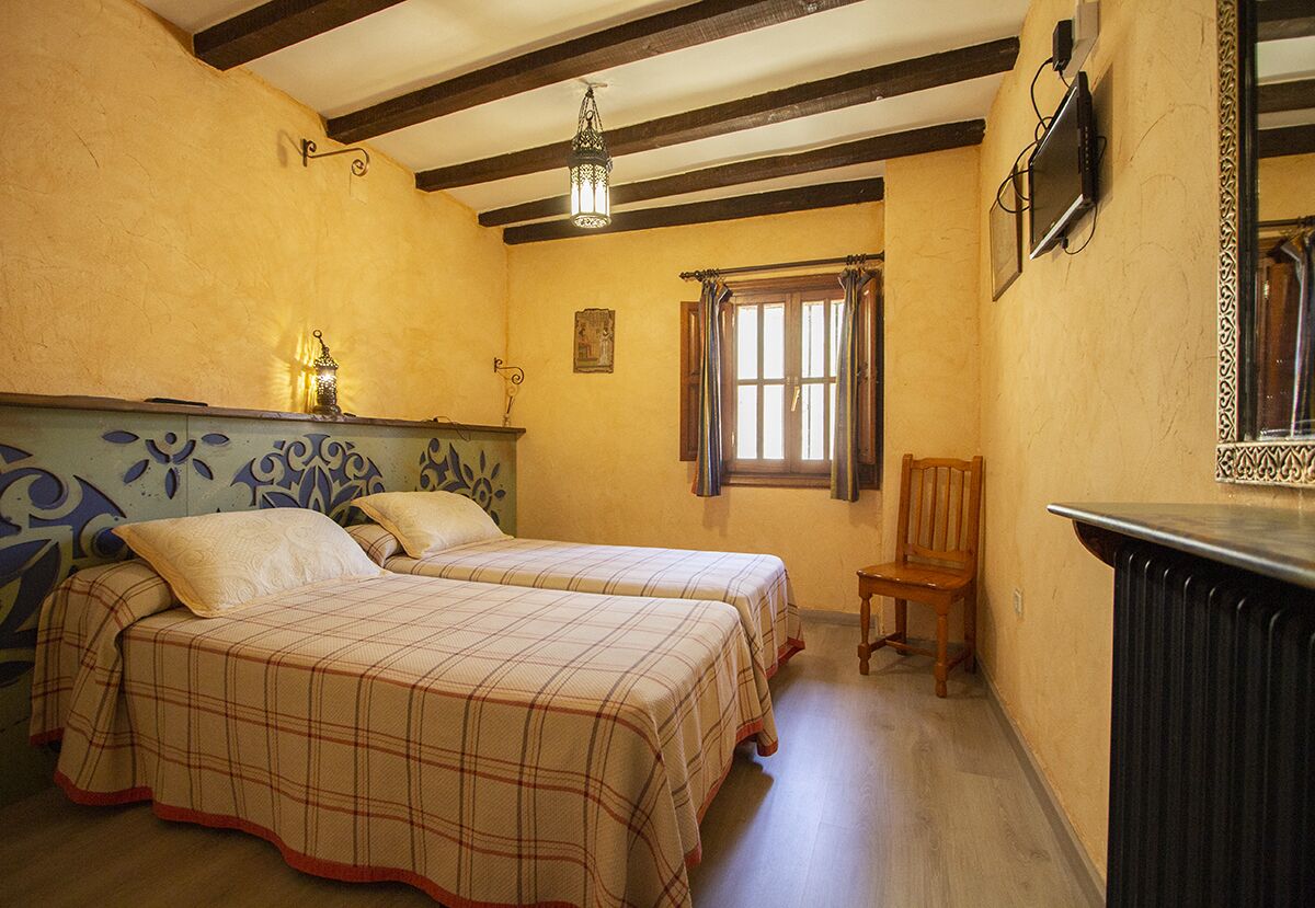 Una habitación con dos camas, una silla de madera, un radiador, un televisor y una ventana con cortinas.