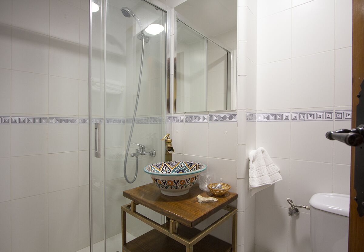 Un baño con ducha de vidrio, lavamanos con un lavabo decorativo y un inodoro blanco.