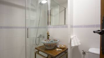 Un baño con ducha de vidrio, lavamanos con un lavabo decorativo y un inodoro blanco.