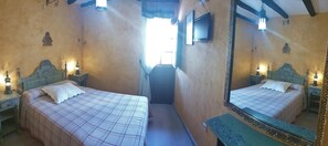 A room with two beds, a television on the wall, and a mirror with a decorative frame.