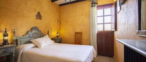 A bedroom with a bed, nightstands, a wooden chair, a window with curtains, and a radiator.