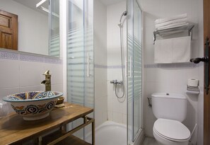 A bathroom with a glass-enclosed shower, a white toilet, and a decorative bowl sink.