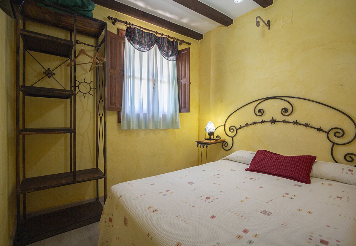 Un dormitori amb un llit, una nitòria, una estantanya penjada a la paret i una finestra amb cortines.