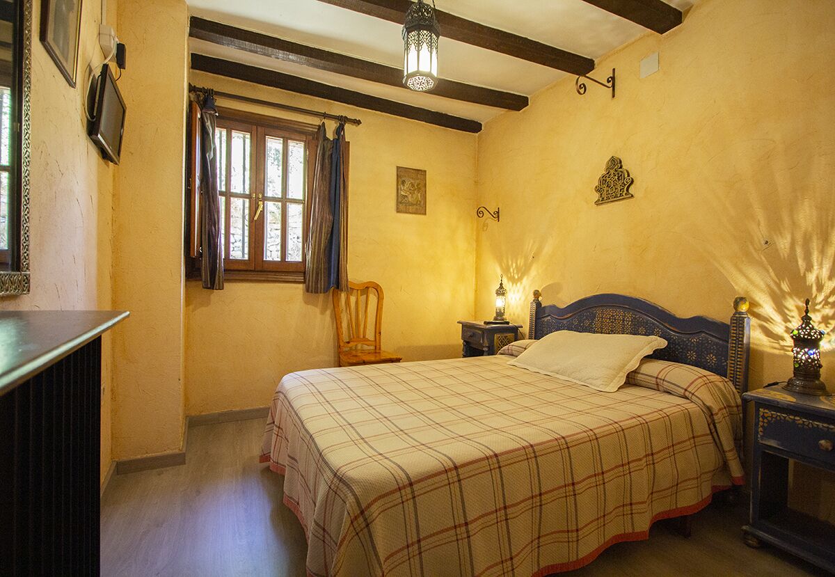 Un dormitorio con cama, mesita de noche, lámpara, ventana con cortinas e iluminación en la pared.