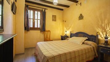 Un dormitorio con cama, mesita de noche, lámpara, ventana con cortinas e iluminación en la pared.