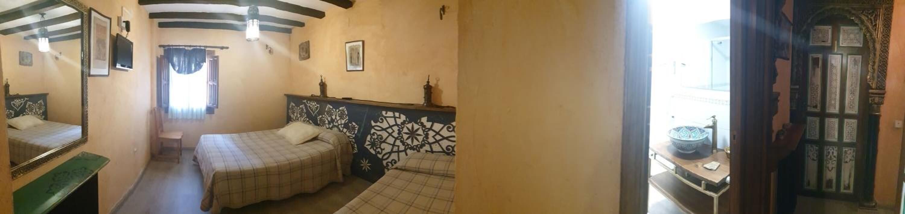 A room with two beds, a mirror, a window with curtains, and a door with intricate designs.