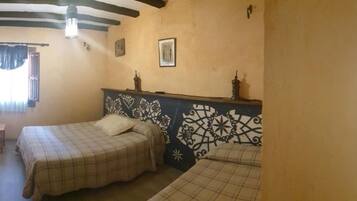 A room with two beds, a mirror, a window with curtains, and a door with intricate designs.