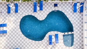 Piscina elevada com piso xadrez, rodeada por espreguiçadeiras e guarda-sóis.