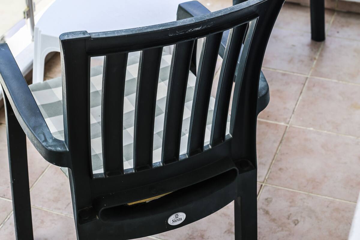 Un balcón con dos sillas negras y una mesa blanca.