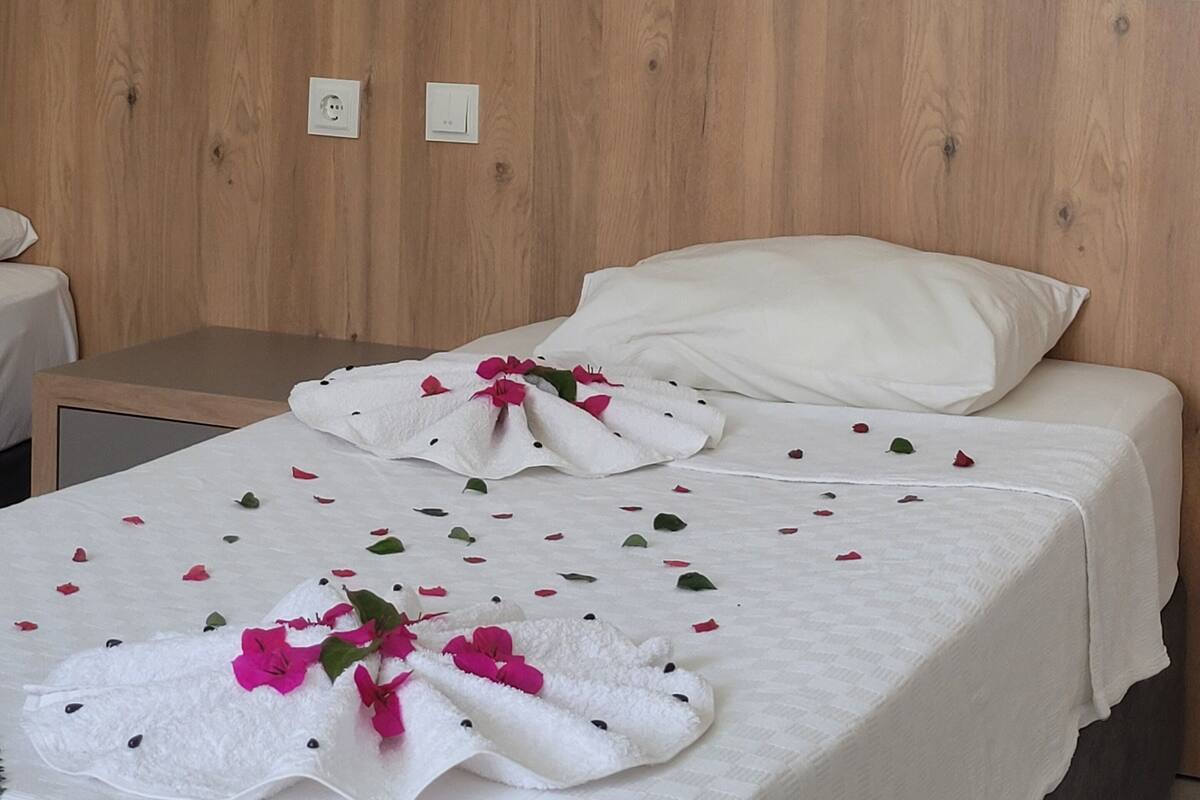 Una cama bien hecha con sábanas blancas y flores rosadas, un cabecero de madera y un cuadro en la pared.