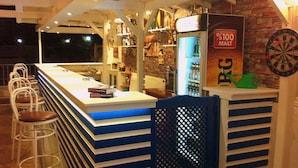 Uma área de bar com banquetas, um alvo de dardos e uma geladeira com uma placa indicando bebida de cevada 100%.