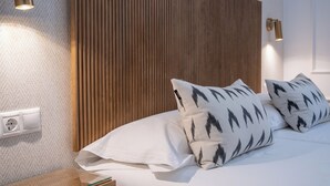 Een keurig opgemaakt bed met witte lakens en gestreepte kussens, een houten hoofdbord en wandlampen.