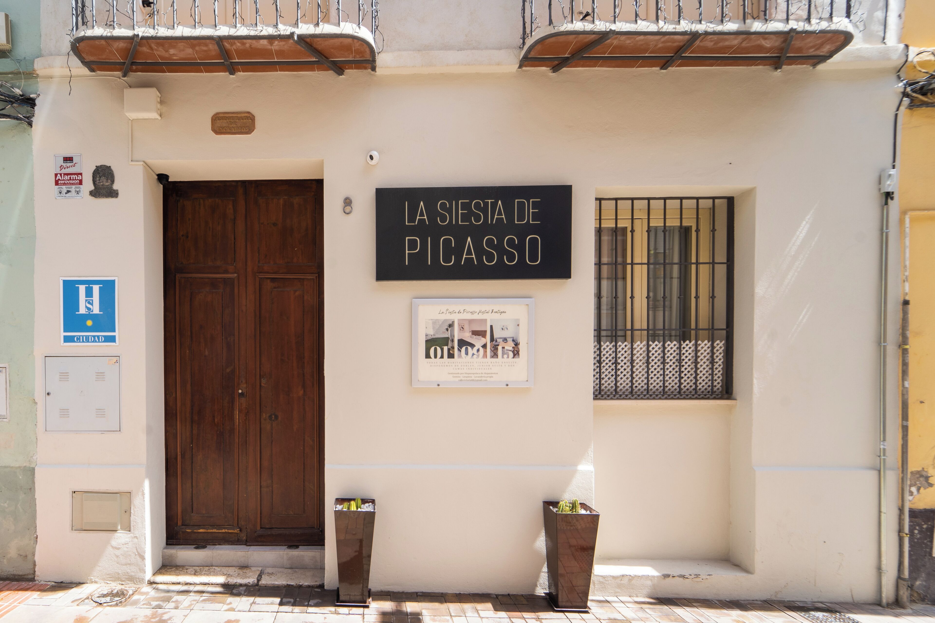 Fachada de edificio con una puerta de madera grande, un cartel que dice 'LA SIERTA DE PICASSO' y dos plantas en macetas.