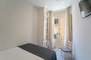 Een slaapkamer met een bed, een stoel en een openslaande balkondeur.