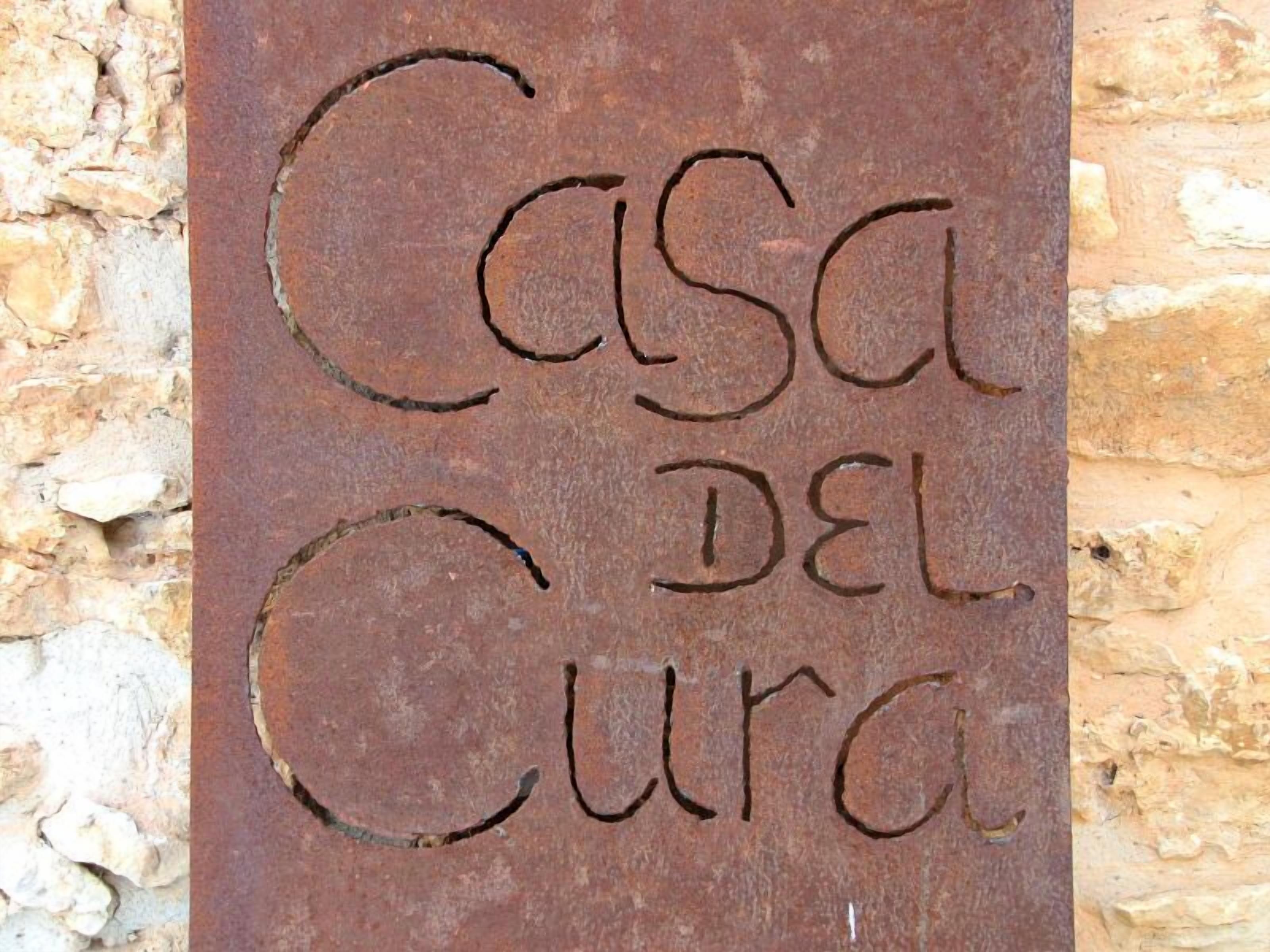 A sign with the text "Casa del Cura" on a stone wall background.