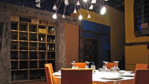 A restaurant with a rustic interior, featuring wooden shelves with bottles, orange chairs, and a table set for dining.