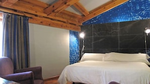 A bedroom with a wooden ceiling, a bed with white linens, a chair, and a nightstand.