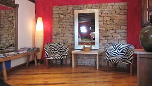A cozy room with a stone wall, a wooden table with magazines, two zebra-patterned chairs, a large mirror, and a floor lamp.