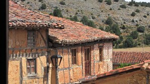 A rustic stone building with a tiled roof, a window with a shutter, and a wall-mounted lantern.