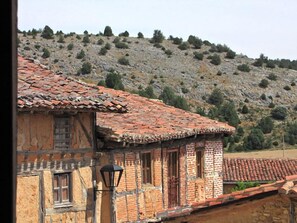 A rustic stone building with a tiled roof, a window with a shutter, and a wall-mounted lantern.