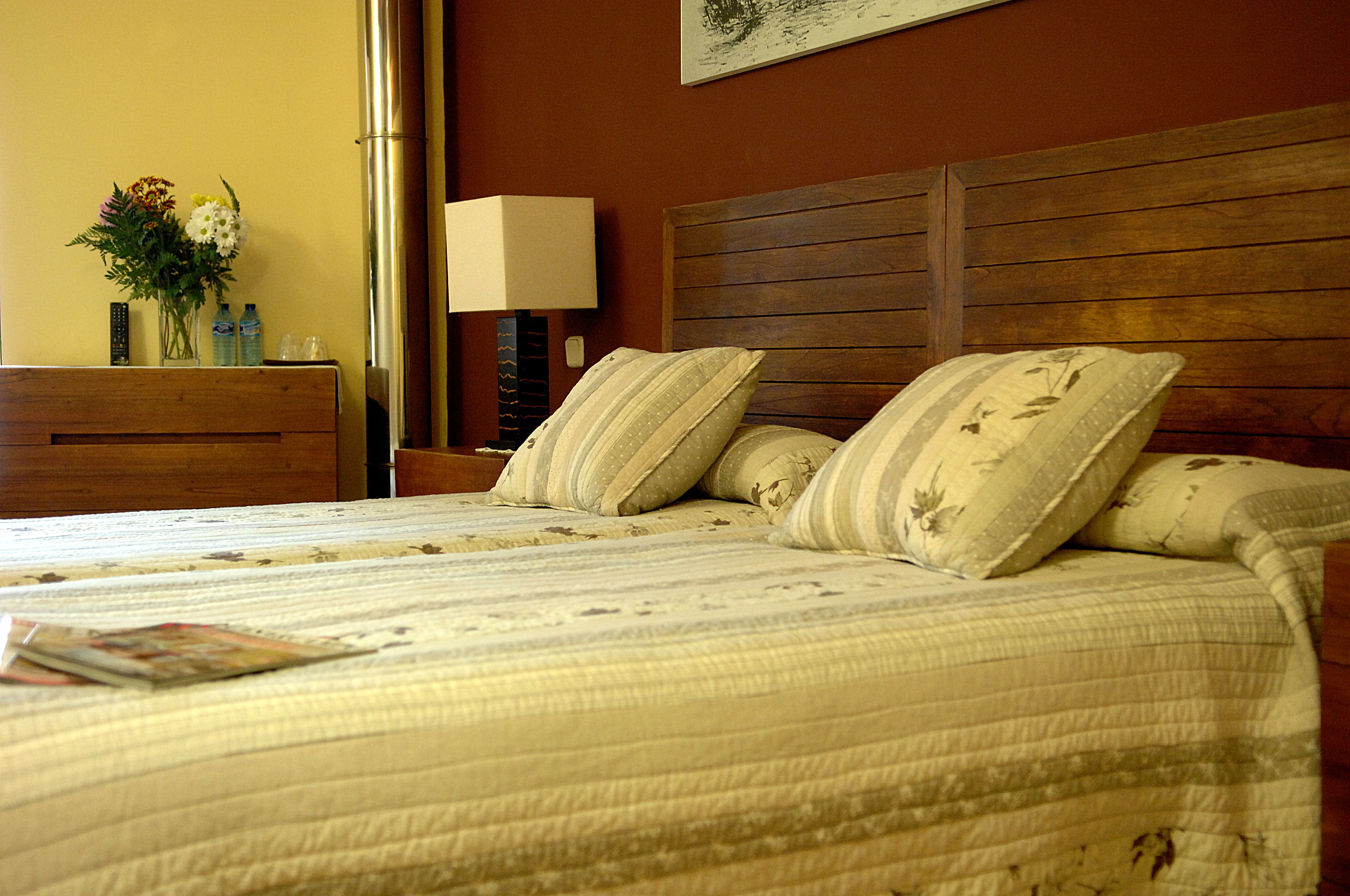 A neatly made bed with floral pillows, a bedside table with a vase of flowers, and a lamp.