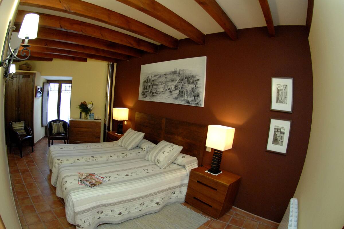 Ein Schlafzimmer mit Holzboden, einem Bett mit zwei Kissen, einem Nachttisch mit Lampe und einem gerahmten Bild an der Wand.