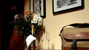 Ein Tisch mit einer Blumenvase, einer Champagnerflasche und zwei Gläsern. Dahinter hängen gerahmte Bilder an der Wand.