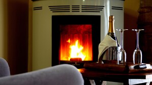 Ein Kamin mit Feuer, eine Champagnerflasche und zwei Weingläser auf einem Holztisch.