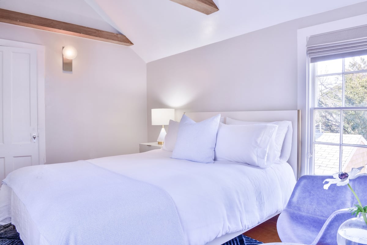 Ein Schlafzimmer mit einem großen Bett, einem Nachttisch mit Lampe, einem Fenster mit Blick und einem Stuhl mit Blume.