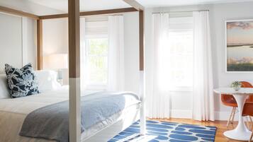 A bedroom with a large bed, a bedside table, a chair, and a window with curtains.
