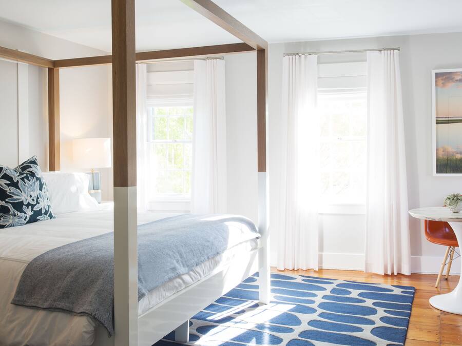 A bedroom with a large bed, a bedside table, a chair, and a window with curtains.