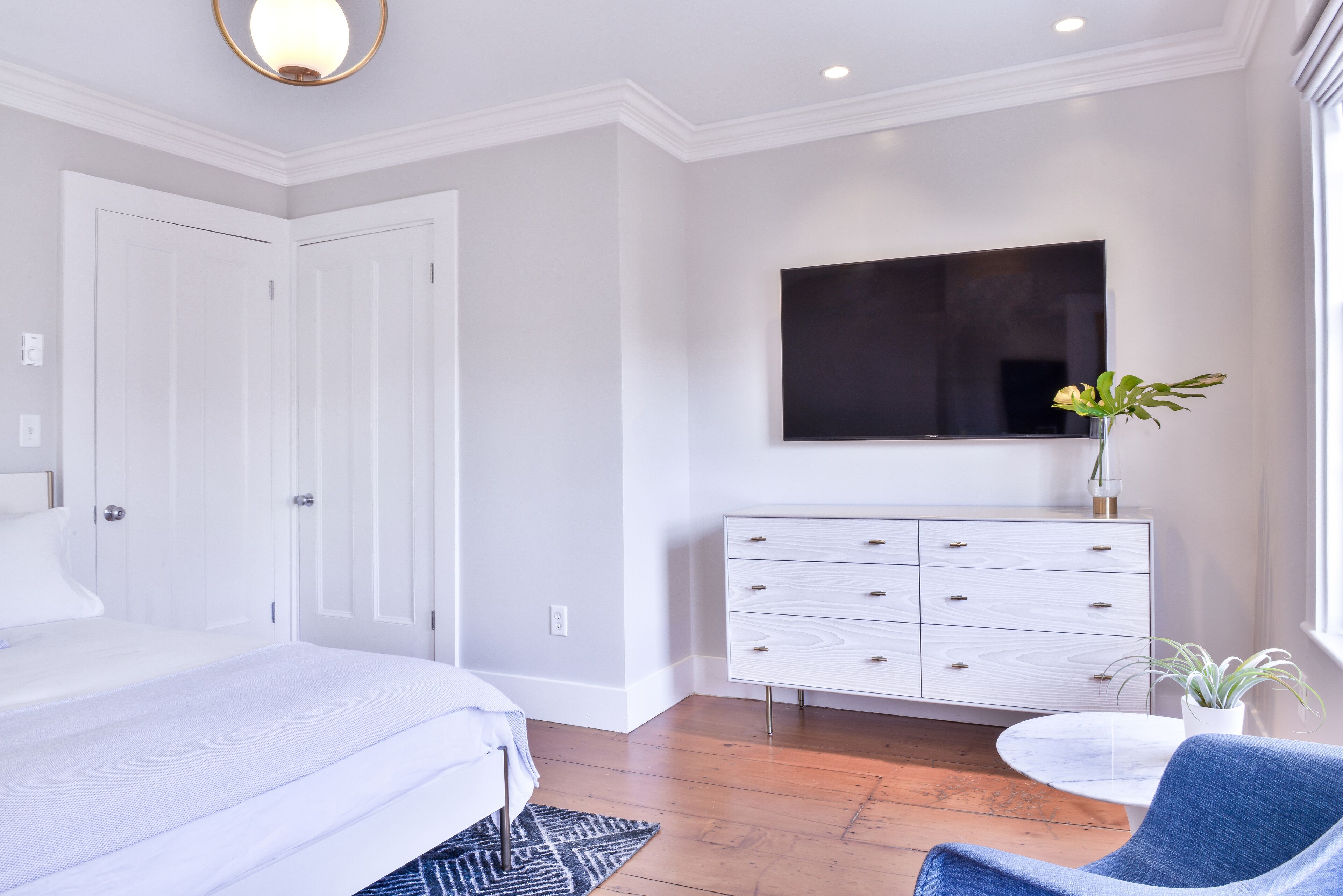 A bedroom with a bed, a dresser, a TV, and a potted plant.