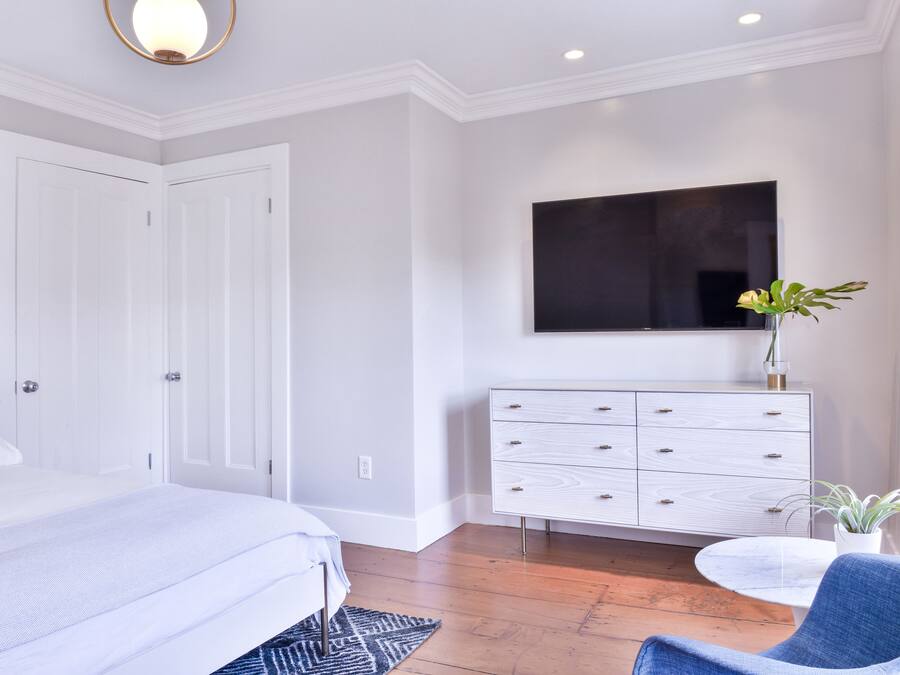 A bedroom with a bed, a dresser, a TV, and a potted plant.