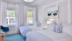 Ein Hotelzimmer mit zwei Betten, einem blauen Sessel, einem Tisch mit Pflanze und Blick ins Freie.