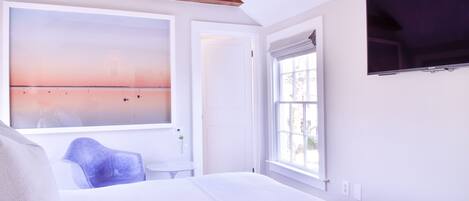 Un dormitorio con un ventanal grande, una cama, un sillón y un televisor montado en la pared.