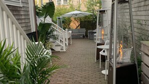 Ein überdachter Patio-Bereich mit einem Ziegelweg, Sitzgelegenheiten im Freien und einer Feuerstelle.