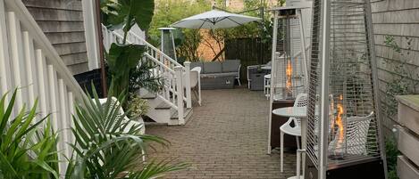 A covered patio area with a brick pathway, outdoor seating, and a fire feature.