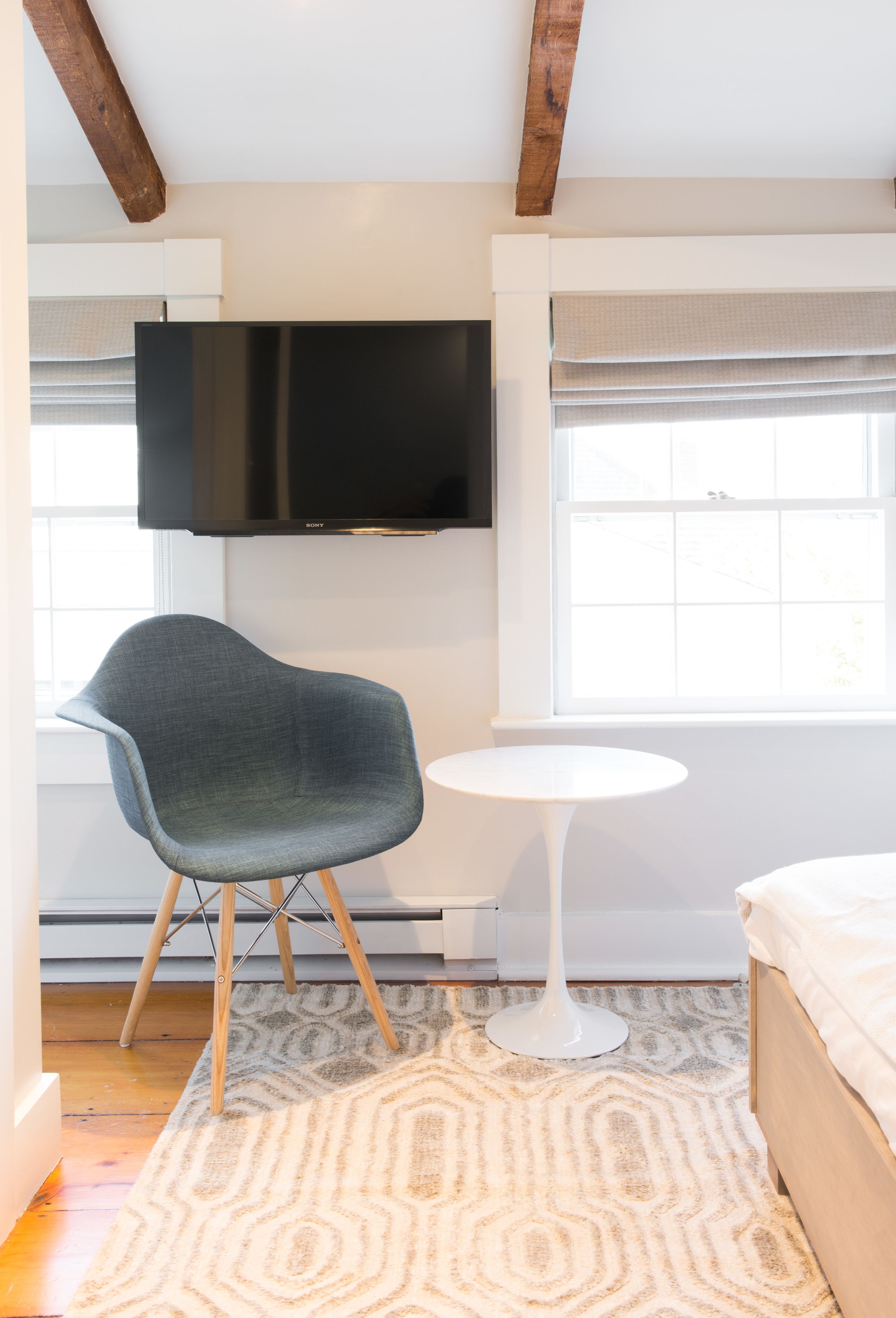 A modern room with a flat-screen TV mounted on the wall, a unique curved chair, a small round table, and a bed with a white headboard.