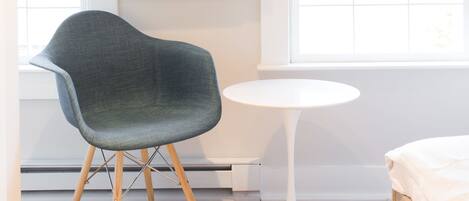 Une chambre moderne dotée d’un téléviseur à écran plat fixé au mur, d’un fauteuil au design original et aux lignes courbes, d’une petite table ronde et d’un lit avec une tête de lit blanche.