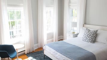 Un dormitorio con cama, mesita de noche, lámpara, silla y ventana con cortinas.