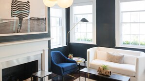 Ein modernes Wohnzimmer mit Kamin, einem blauen Sessel, einem weißen Sofa und großen Fenstern.