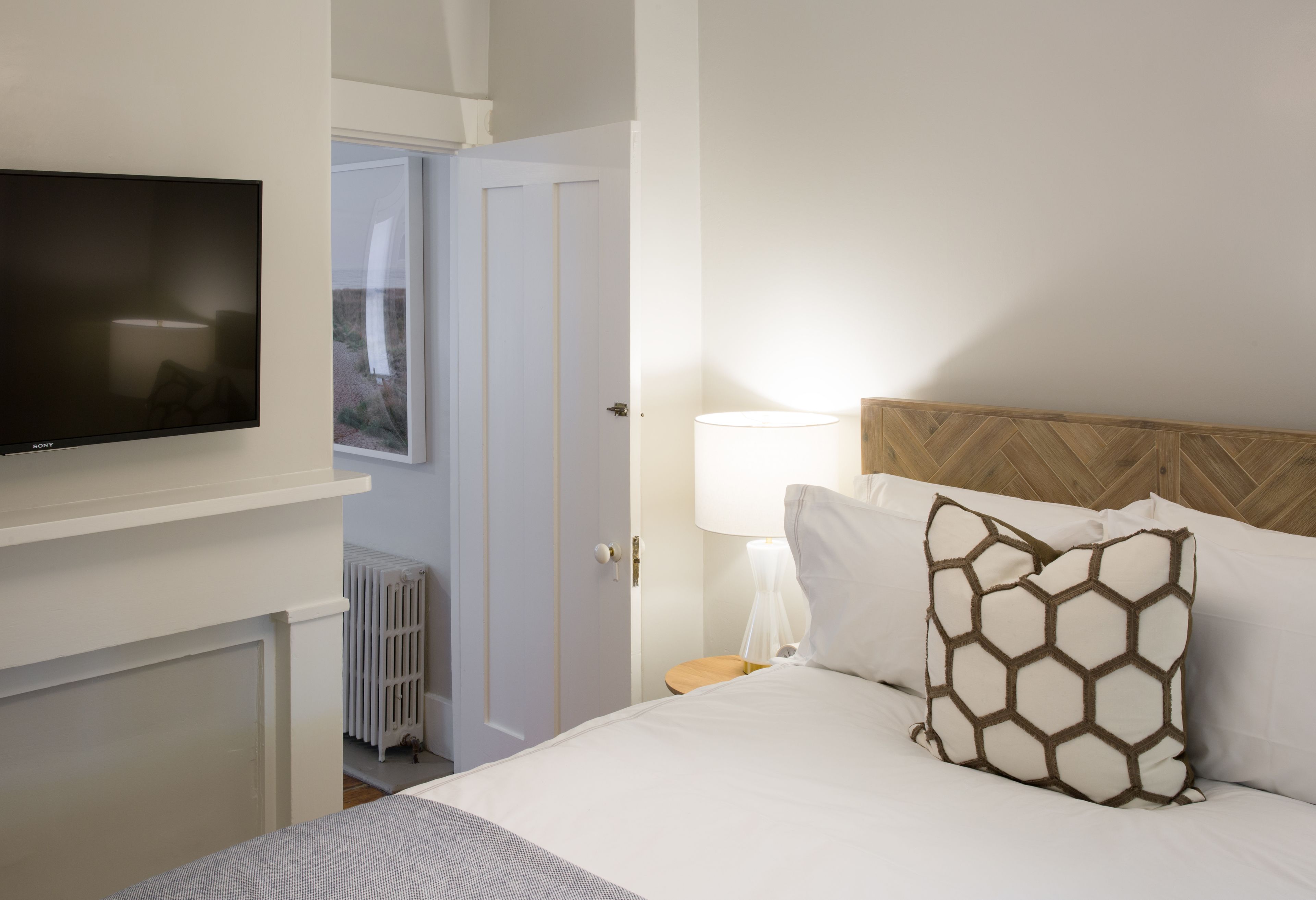 Quarto de hotel com cama, televisão, luminária e porta que dá para uma varanda.