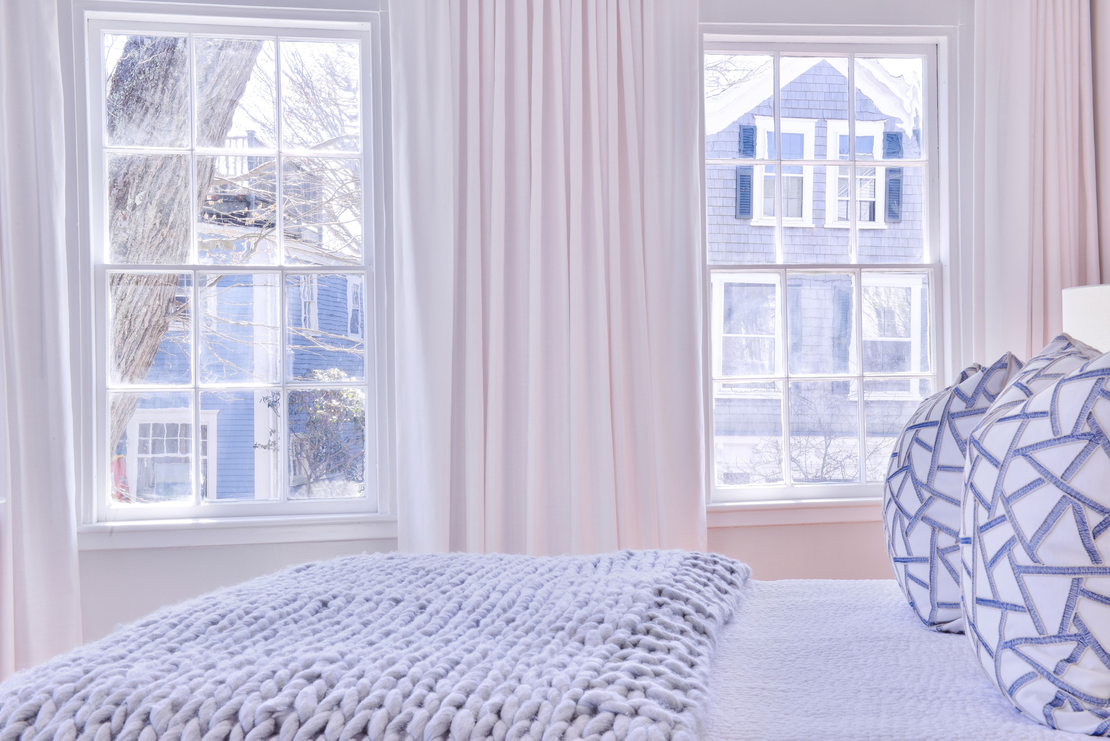 Un dormitorio con un ventanal grande, una cama con ropa de cama blanca y una almohada estampada.