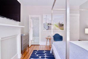 Un dormitorio moderno con una cama, un televisor montado en la pared, una mesita auxiliar y vistas al exterior a través de una ventana.