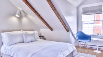 Ein Schlafzimmer mit schrägem Dach, einem Bett mit weißer Bettwäsche, einem blauen Sessel und einem kleinen Tisch.