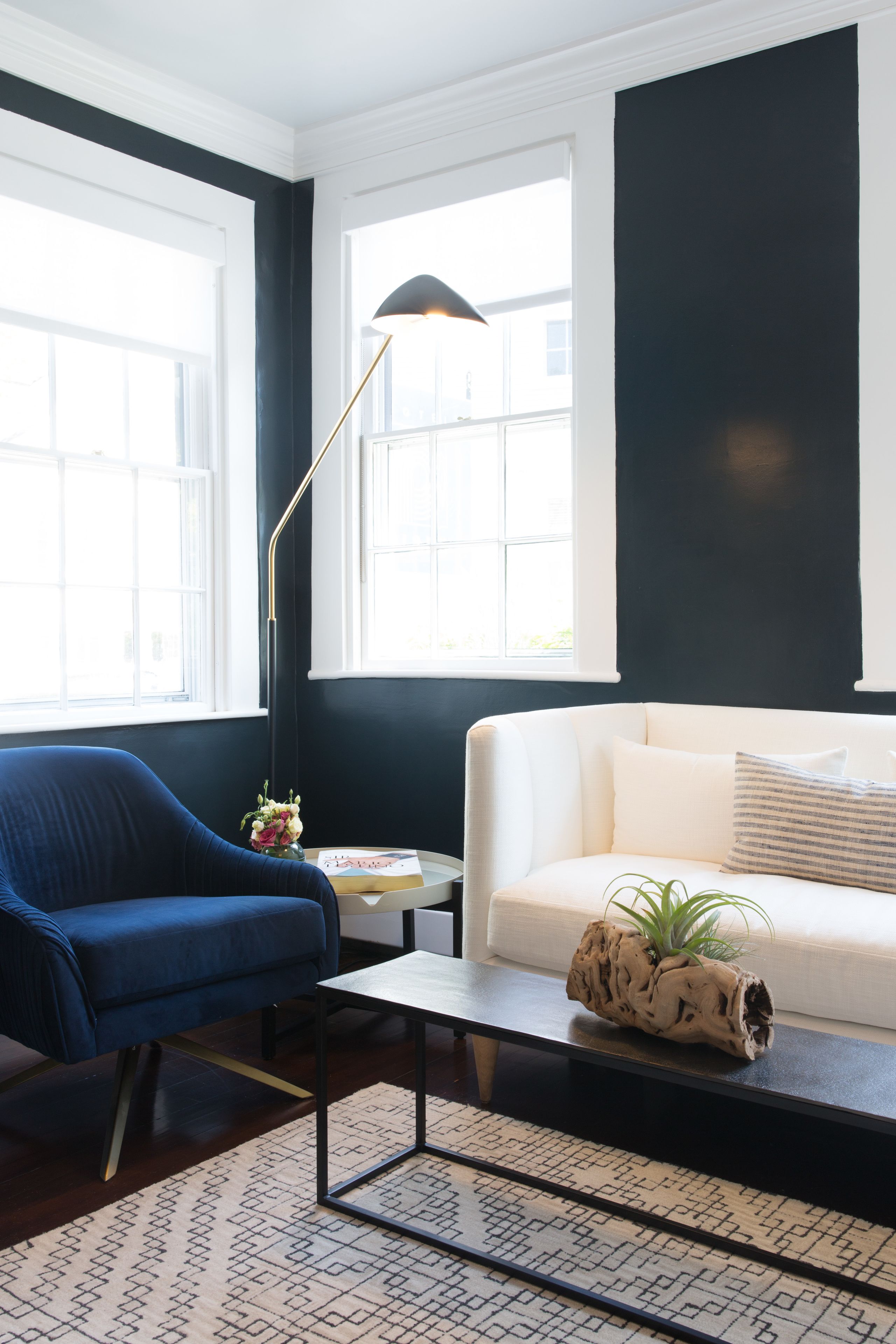 A modern living room with a blue armchair, a white sofa, a black floor lamp, and a patterned rug.