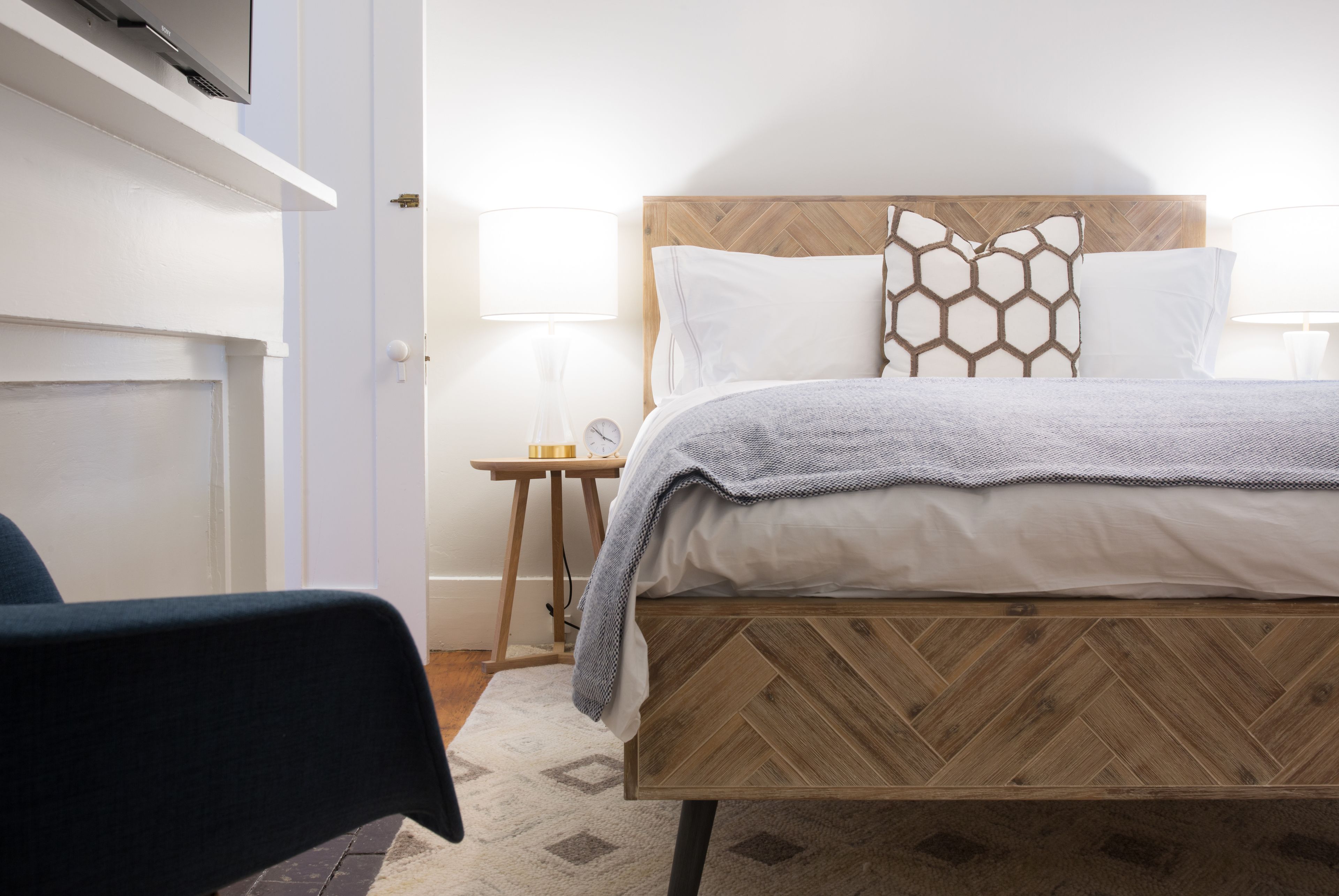 Une chambre à coucher avec une tête de lit en bois, un lit recouvert de linge de lit blanc, une petite table de chevet avec une lampe et une chaise.