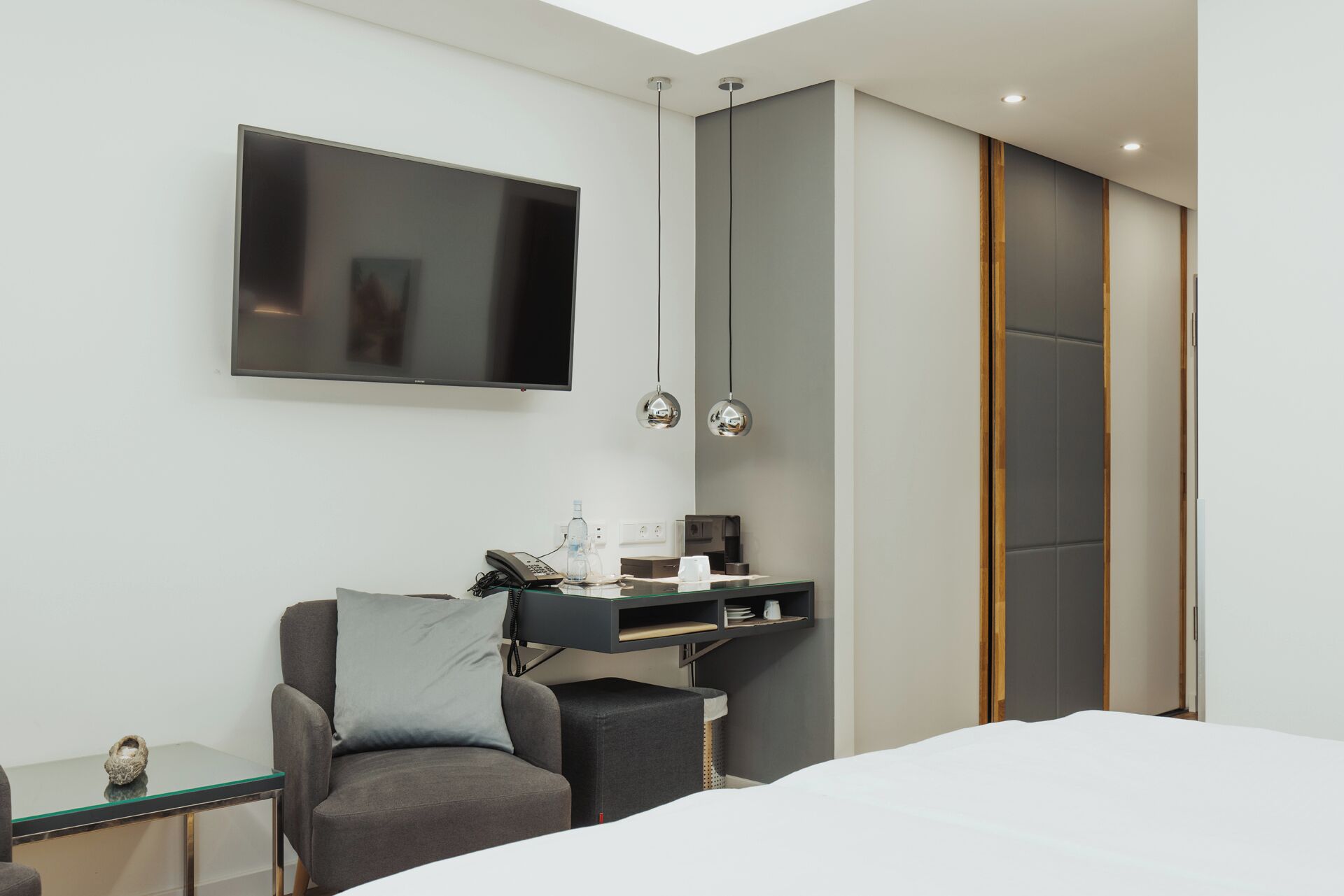 A modern hotel room with a large bed, a desk with a chair, a flat-screen TV, and a minibar.